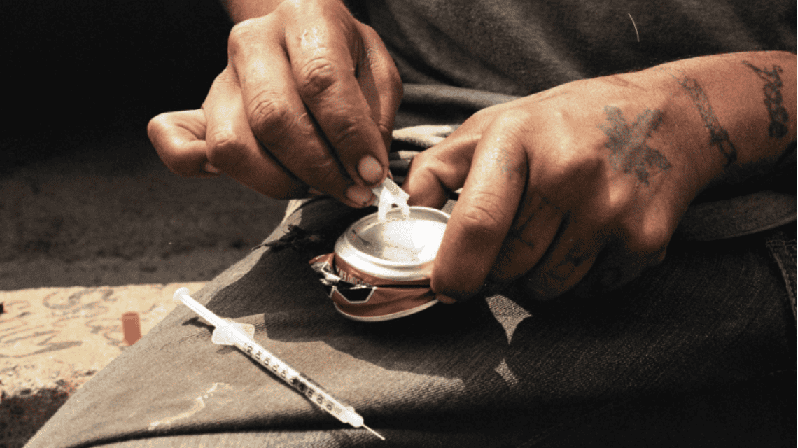 Fotografía de las manos de una persona preparandose para inyectarse heroina con una jeringa