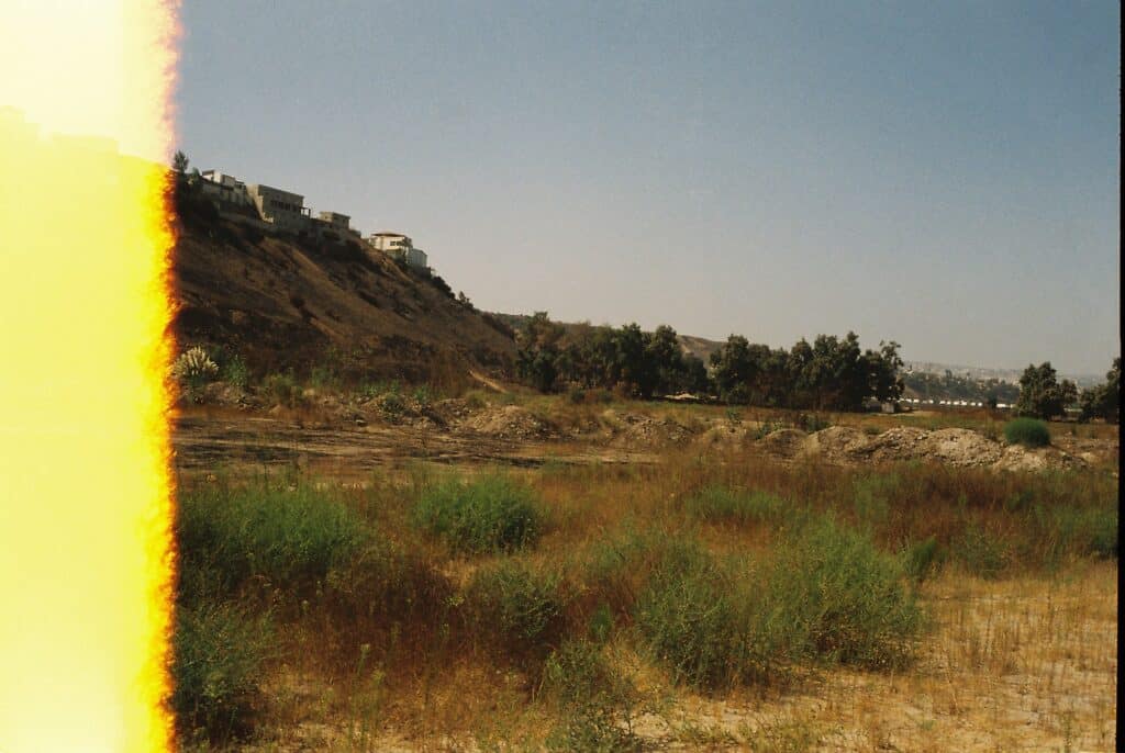 Fotografía: Vista de montículos de tierra en un terreno. Al fondo a la izquierda se ven casas. 
