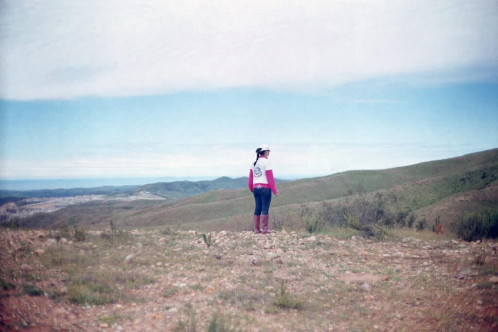 Fotografía: Mujer buscadora de espaldas. Al fondo se ve el paisaje, montañas y llanura. 