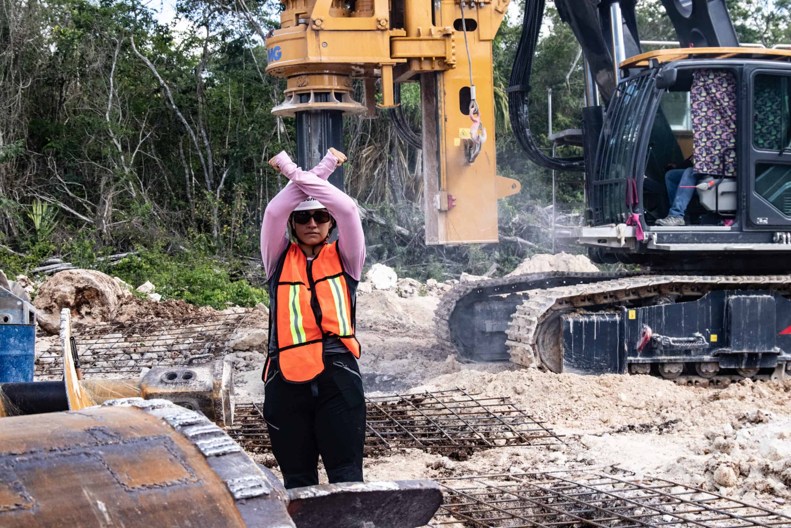 Fotografía de una mujer frente a maquinaria pesada, haciendo una señal de protesta ante la construcción del Tren Maya